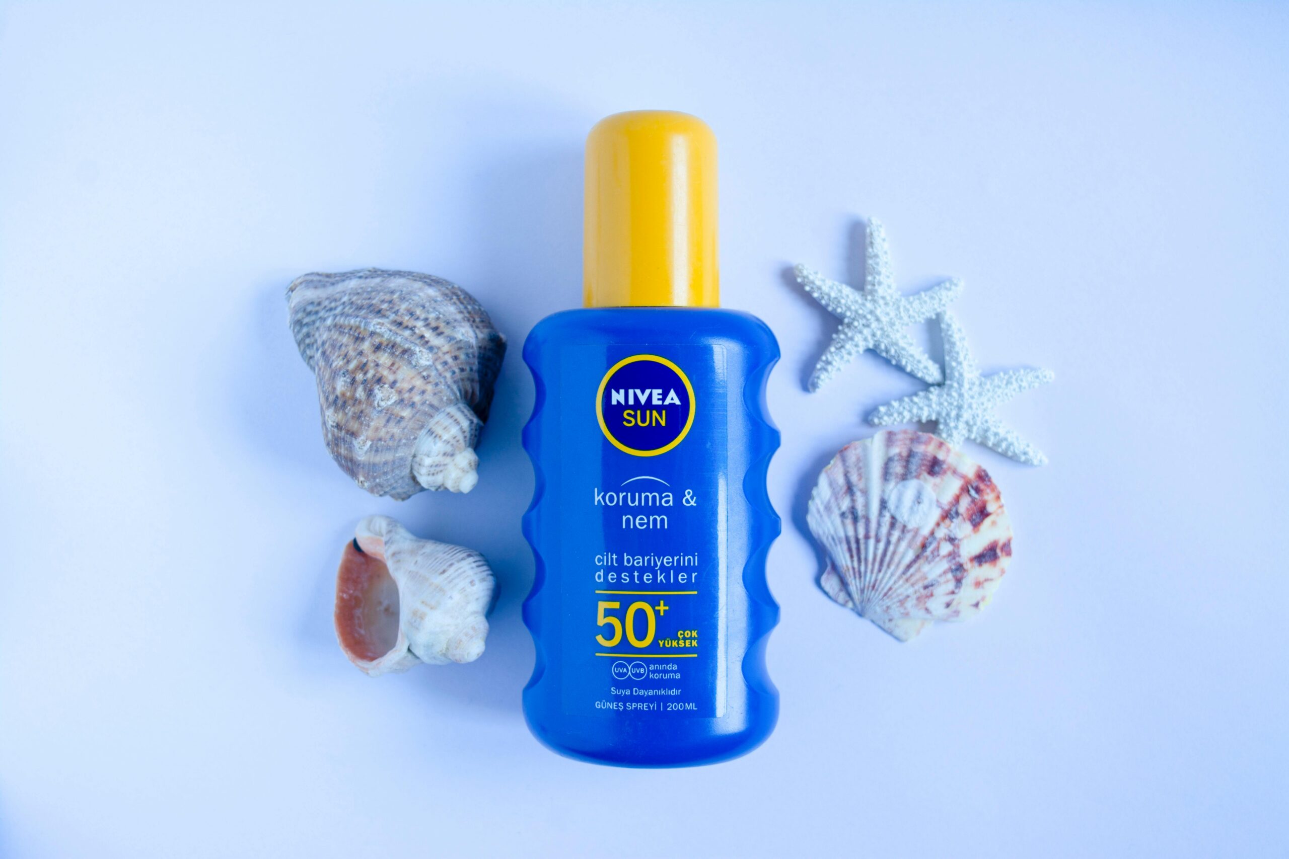 Blue Nivea Sun SPF 50+ sunscreen bottle on white background with seashells and starfish for summer skincare.
