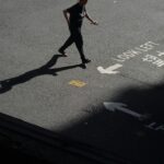 A person walks on a Hong Kong street casting a long shadow, with road markings in Chinese and English.