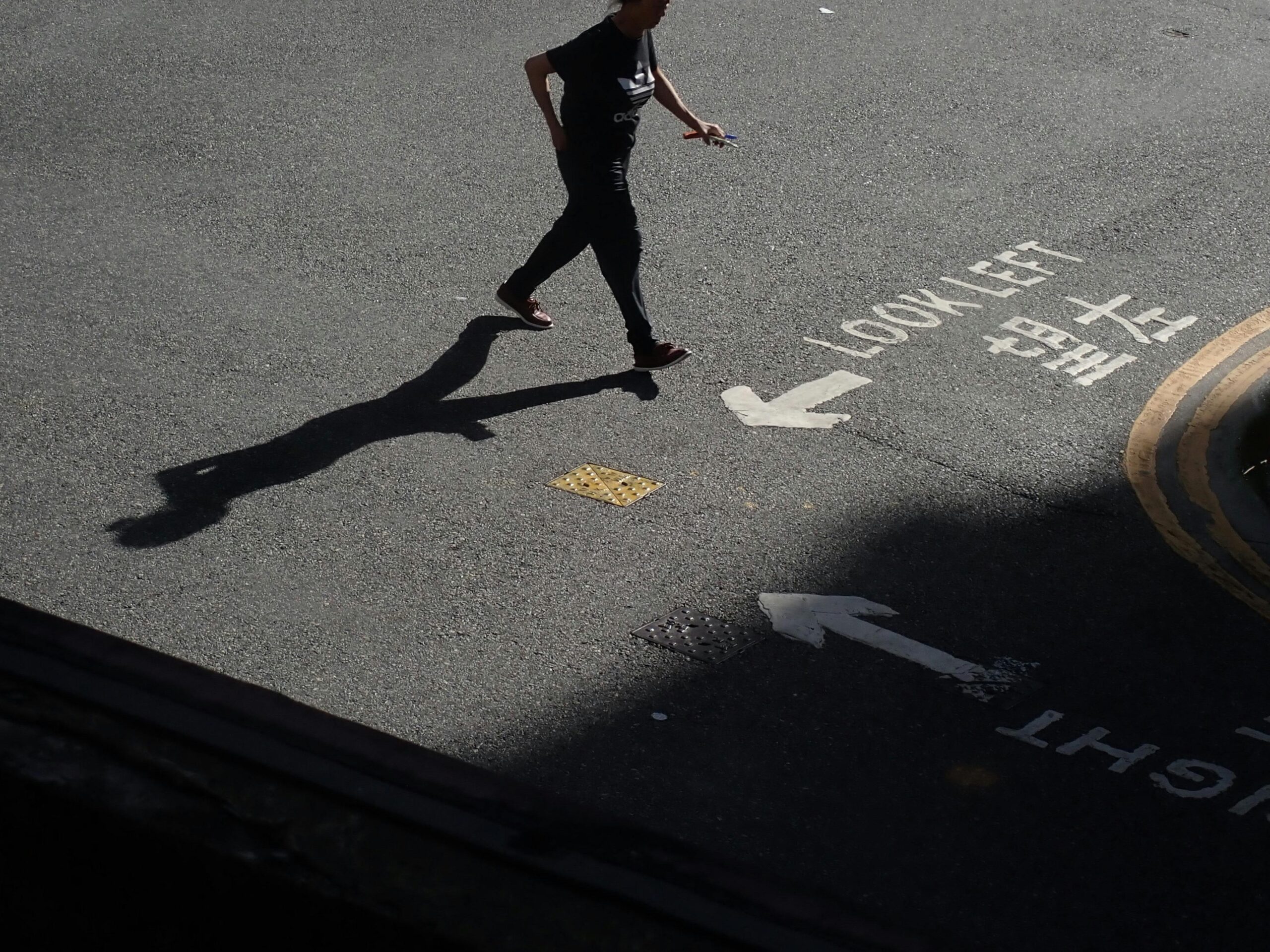 A person walks on a Hong Kong street casting a long shadow, with road markings in Chinese and English.