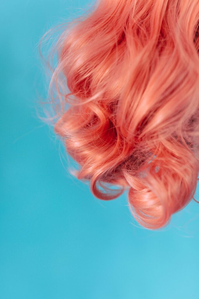 Close-up of vibrant pink curly hair against a teal blue background. Bold and stylish.