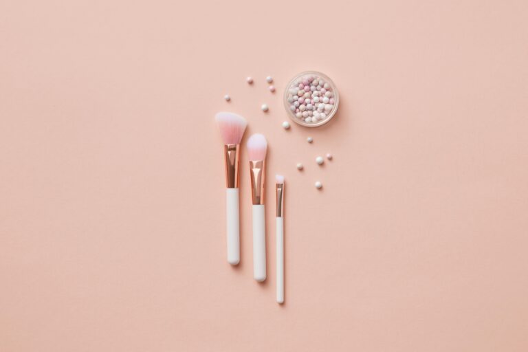 Why You Should Clean Your Makeup Brushes & How to Do It Right Flat lay of makeup brushes and pearlescent powder balls on a beige background. Ideal for beauty and cosmetic themes.