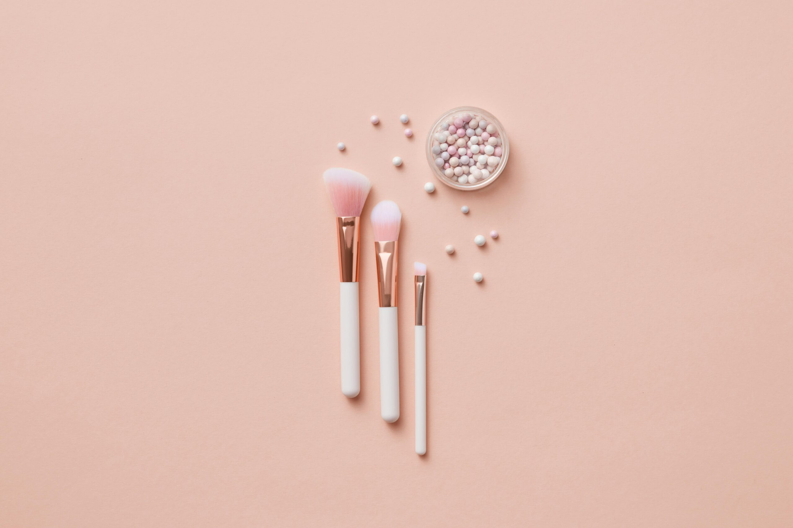 Flat lay of makeup brushes and pearlescent powder balls on a beige background. Ideal for beauty and cosmetic themes.