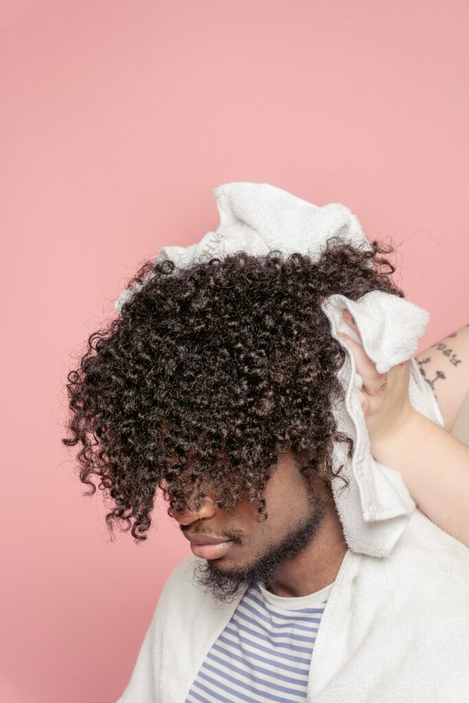 Man with curly hair being attended to in a salon setting with a pink background.